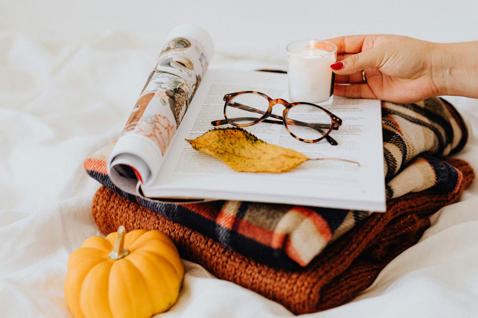 Close-up of folded fabrics, glasses, candle, and pumpkin for a cozy fall setup.